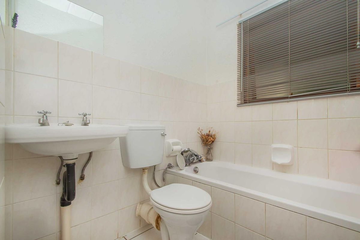 A functional bathroom featuring a pedestal basin, standard toilet, and bathtub with tiled walls and window blinds.