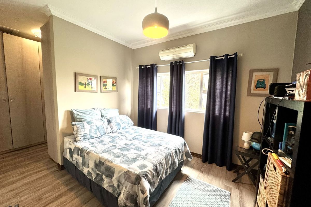 A well-maintained bedroom featuring laminate flooring, built-in cupboards, and a wall-mounted split-system air conditioner for climate control.