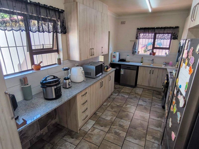 Functional kitchen featuring light wood-look cabinetry, granite countertops, tiled flooring, and double basin sink with security bars on windows.