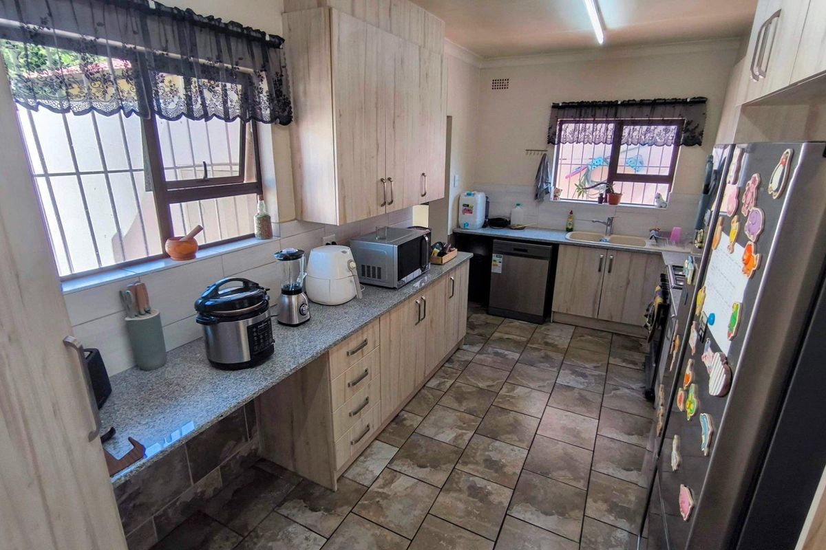 Functional kitchen featuring light wood-look cabinetry, granite countertops, tiled flooring, and double basin sink with security bars on windows.
