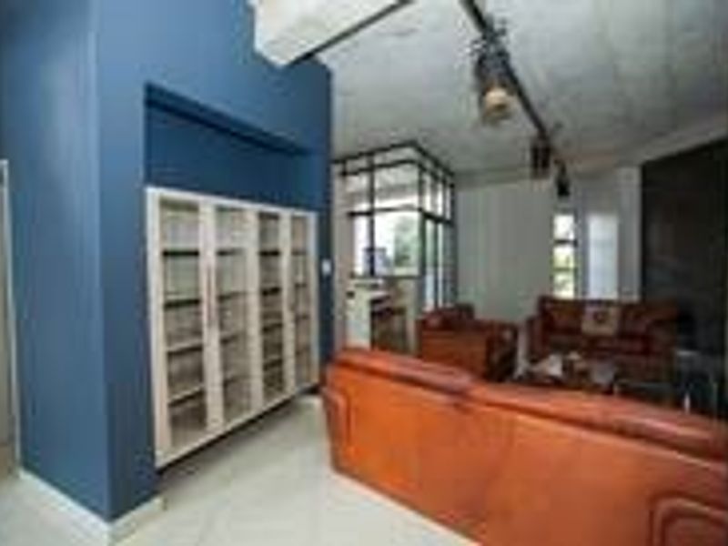Spacious living area featuring built-in shelving, industrial-style track lighting, and an exposed concrete ceiling with neutral tiled flooring.