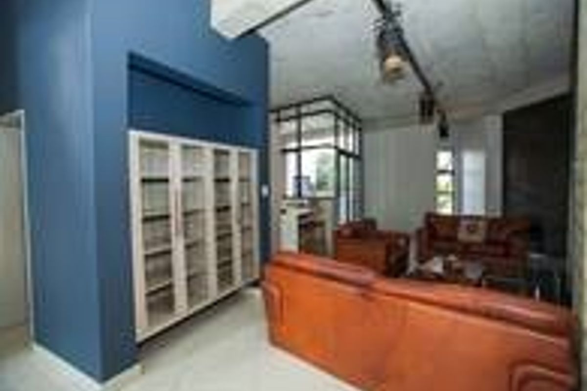 Spacious living area featuring built-in shelving, industrial-style track lighting, and an exposed concrete ceiling with neutral tiled flooring.
