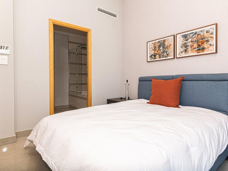 A well-maintained bedroom featuring tiled flooring, ducted air conditioning, and direct access to an en-suite bathroom with a glass-enclosed shower.