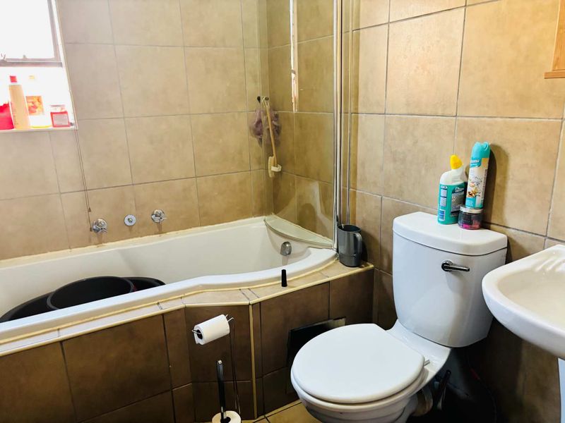 A functional bathroom featuring a built-in bathtub with a glass screen, pedestal basin, and toilet, finished with neutral ceramic wall and floor tiling.