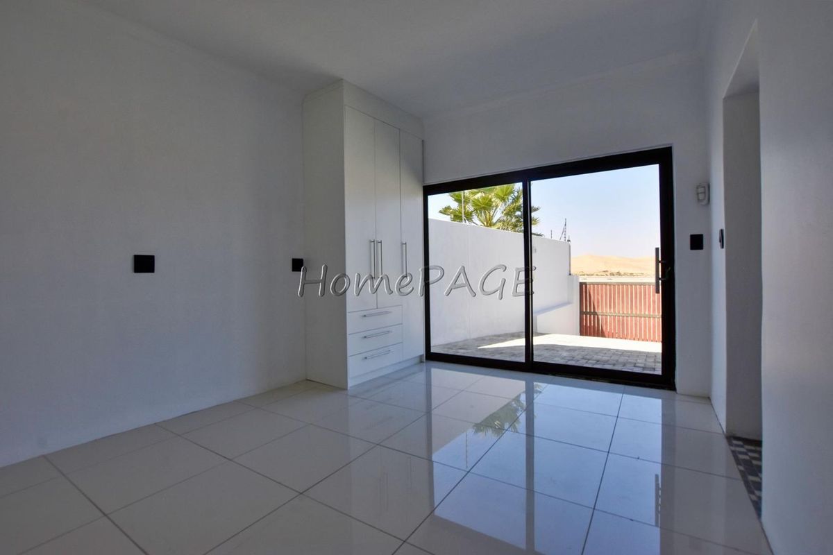 A bright, modern bedroom featuring white tiled flooring, built-in cabinetry, and large sliding glass doors providing direct access to an outdoor patio area.