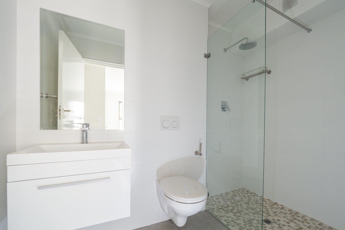 Modern bathroom featuring a wall-mounted vanity, a frameless glass walk-in shower with mosaic tile flooring, and a wall-hung toilet.
