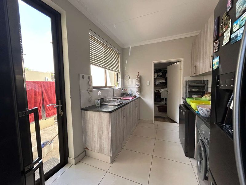 A functional scullery area featuring built-in cabinetry, laminate countertops, a stainless steel sink, and direct access to the exterior.