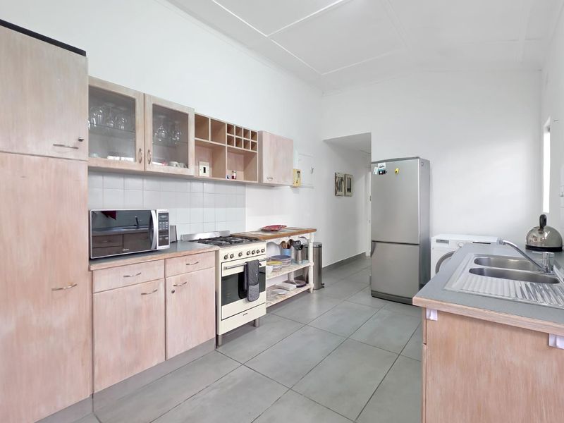 Functional kitchen featuring light wood-tone cabinetry, gas stove with oven, tiled backsplash, and double bowl sink with tiled flooring throughout.