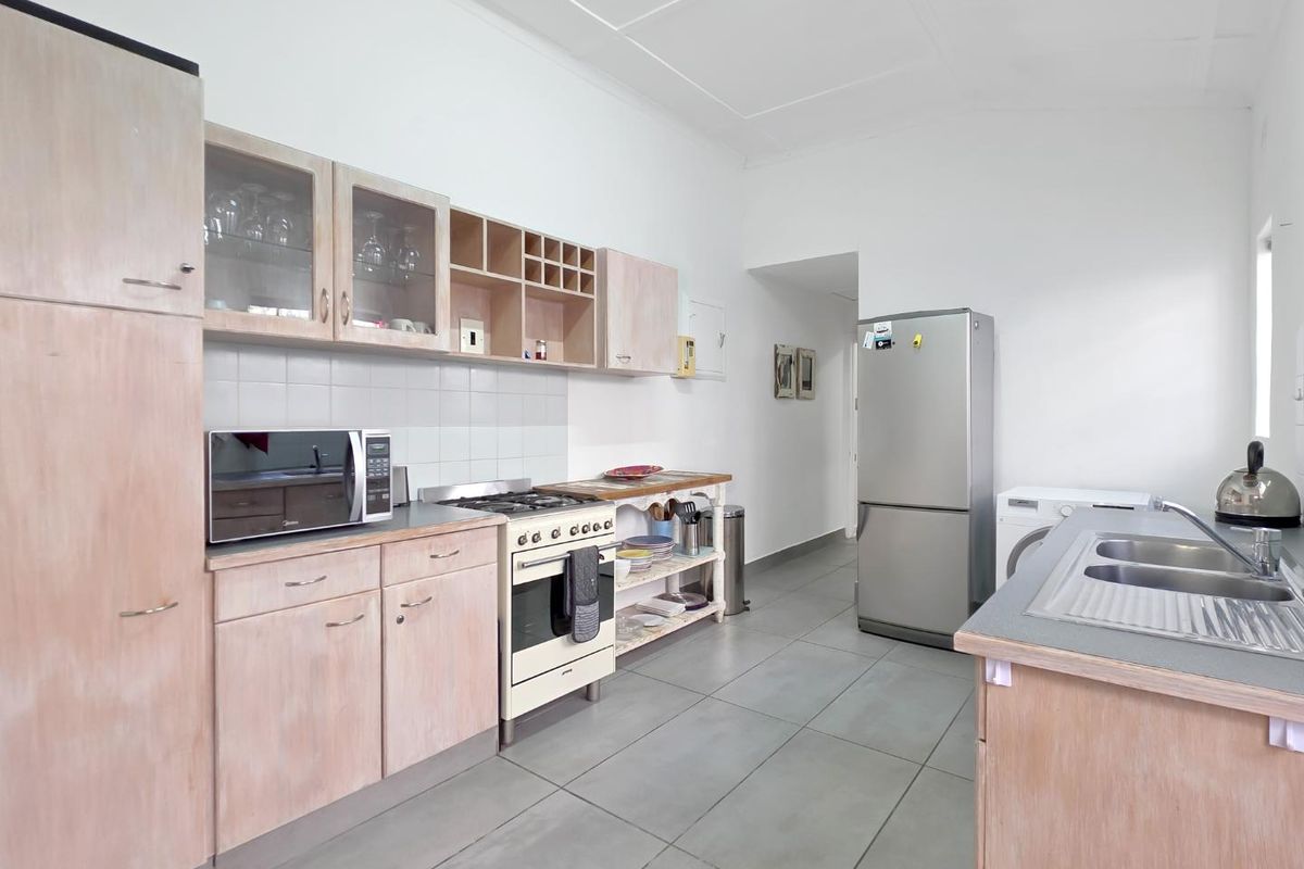 Functional kitchen featuring light wood-tone cabinetry, gas stove with oven, tiled backsplash, and double bowl sink with tiled flooring throughout.