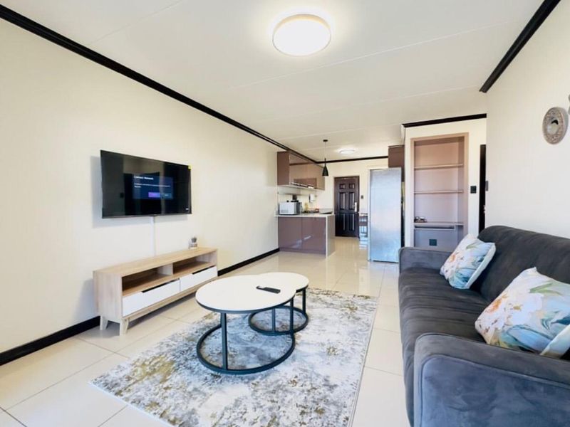 Open-plan living area featuring tiled flooring, a modern kitchen with built-in cabinetry, and integrated shelving, creating a functional and cohesive living space.