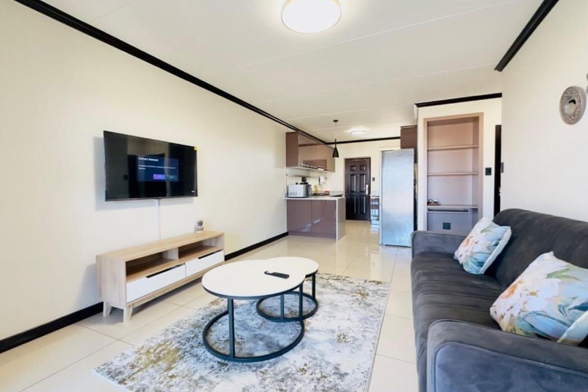 Open-plan living area featuring tiled flooring, a modern kitchen with built-in cabinetry, and integrated shelving, creating a functional and cohesive living space.