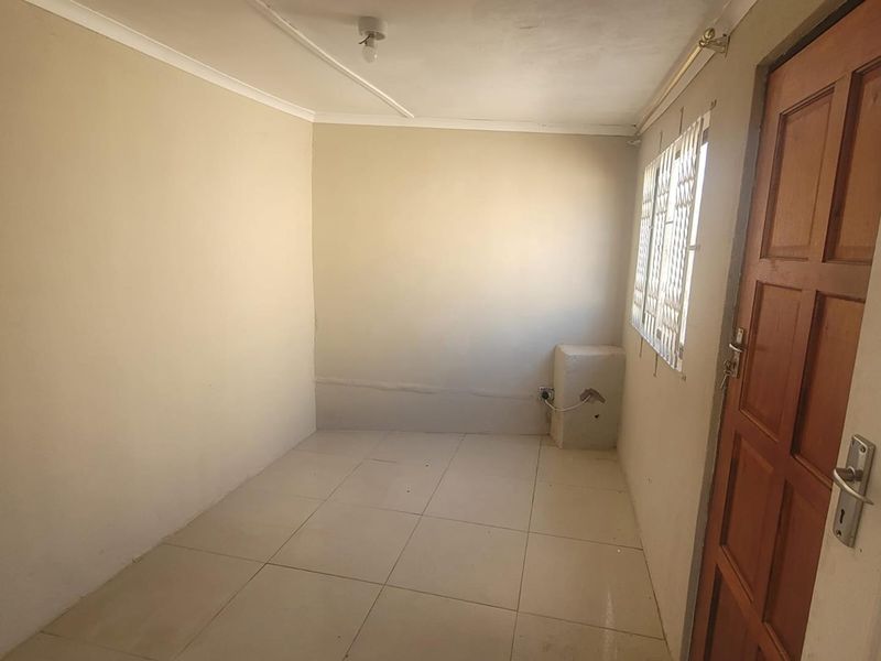 An empty bedroom featuring tiled flooring, a timber door, and a window with security bars. The room requires minor wall repairs and cosmetic updates.