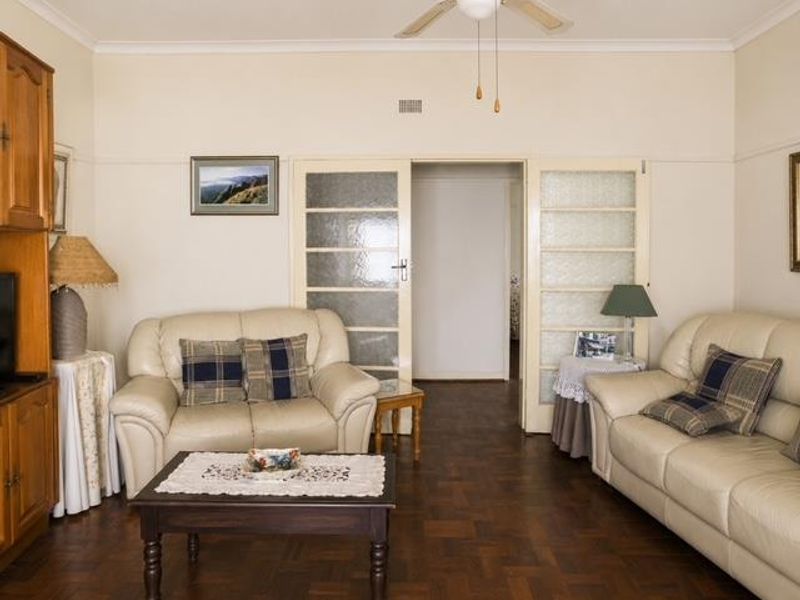 A traditional living room featuring classic parquet flooring, a ceiling fan, and double glass panel doors leading to an adjacent space.