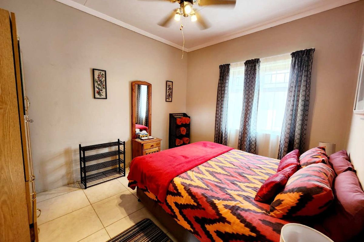 A well-lit bedroom featuring tiled flooring, a ceiling fan, and large windows that provide natural light.