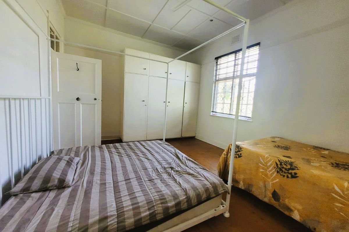 A bedroom featuring built-in wardrobes, timber flooring, and a window with security bars.