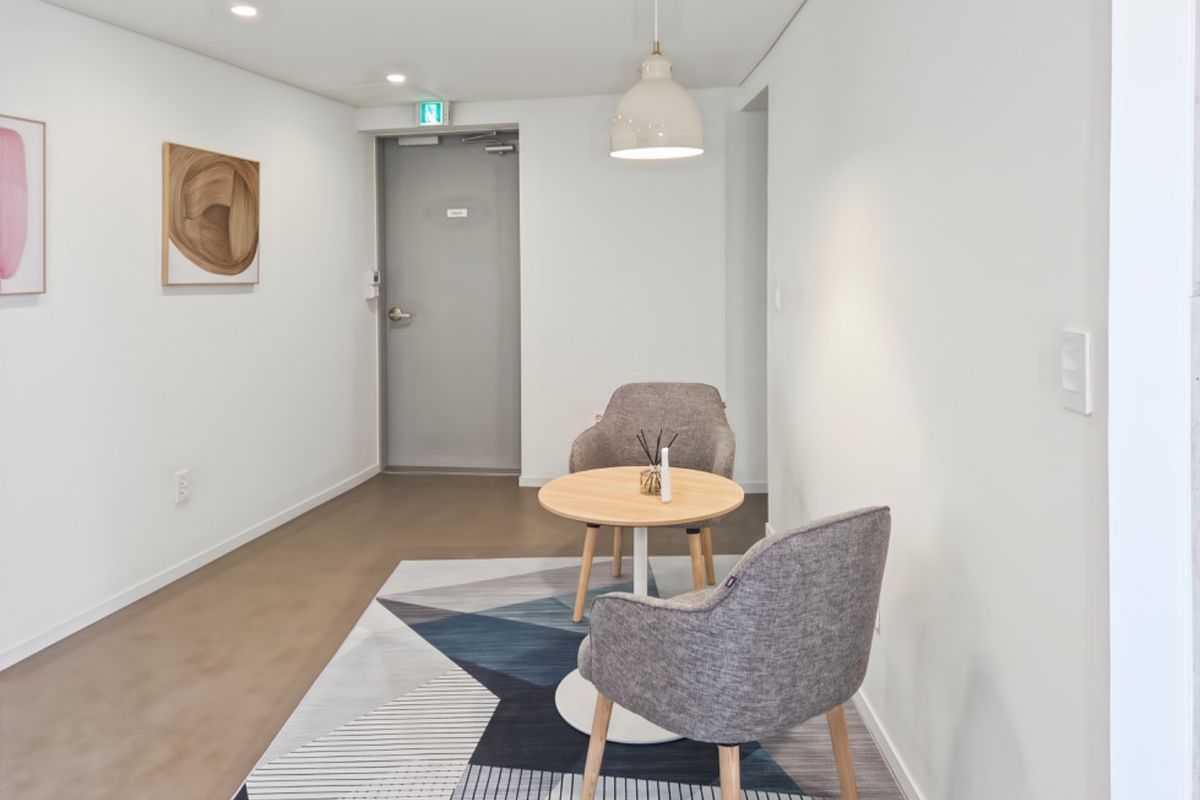 A bright and modern office breakout area featuring clean white walls, recessed lighting, and a contemporary pendant light fixture.