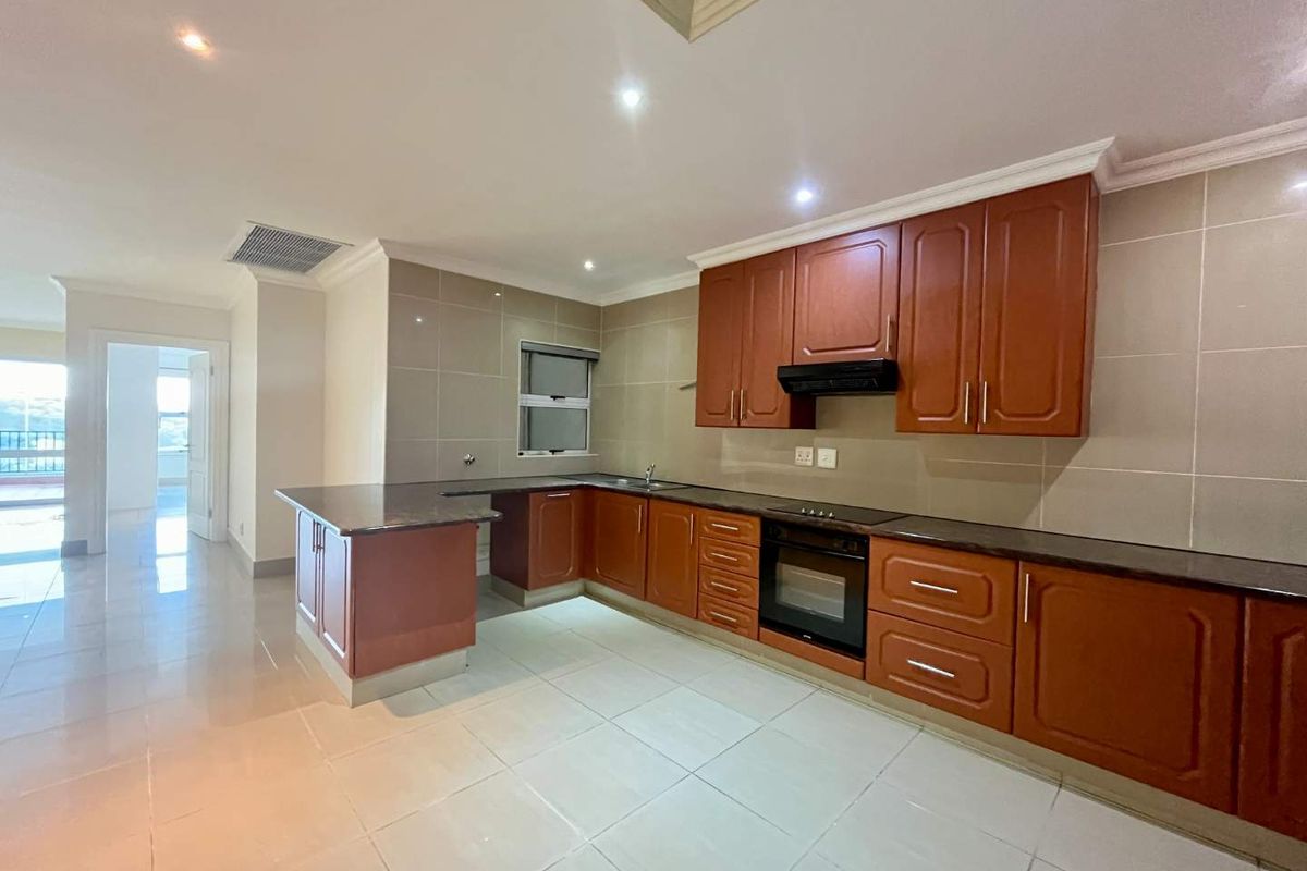 Spacious kitchen featuring dark wood cabinetry, granite countertops, integrated appliances, and neutral tiled flooring, offering a clean and functional layout.