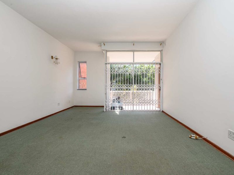 An empty living room featuring carpet flooring, a security gate, and a sliding glass door leading to an outdoor area.
