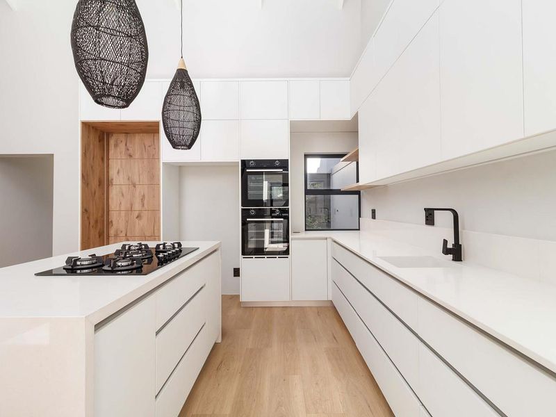 Modern kitchen featuring sleek white cabinetry, stone countertops, a central island with a gas cooktop, and high-end built-in double ovens.