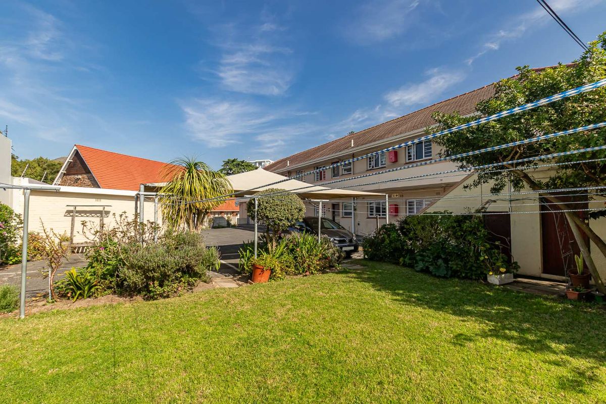A view of the rear exterior of the apartment complex, featuring a shared lawn area, paved driveway, and installed shade sail structure.