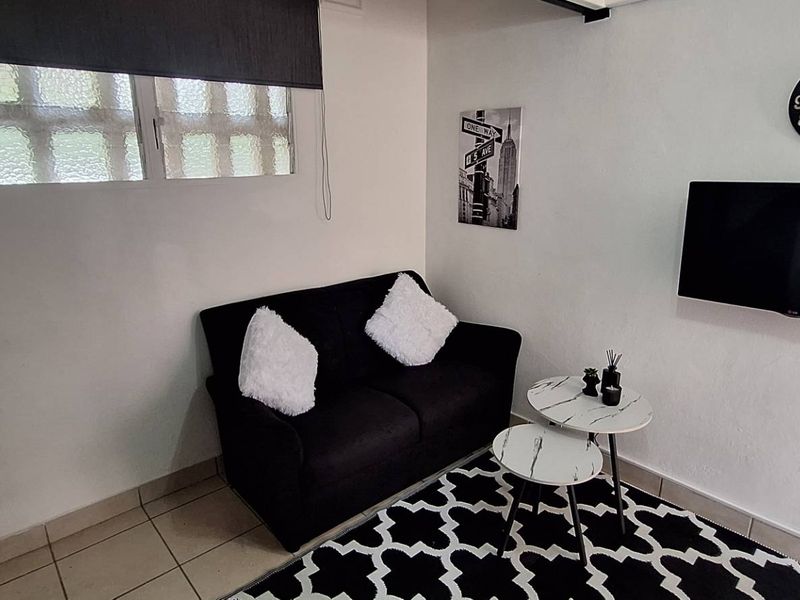 A compact living area featuring tiled flooring and a window with a roller blind, providing a functional space for relaxation.