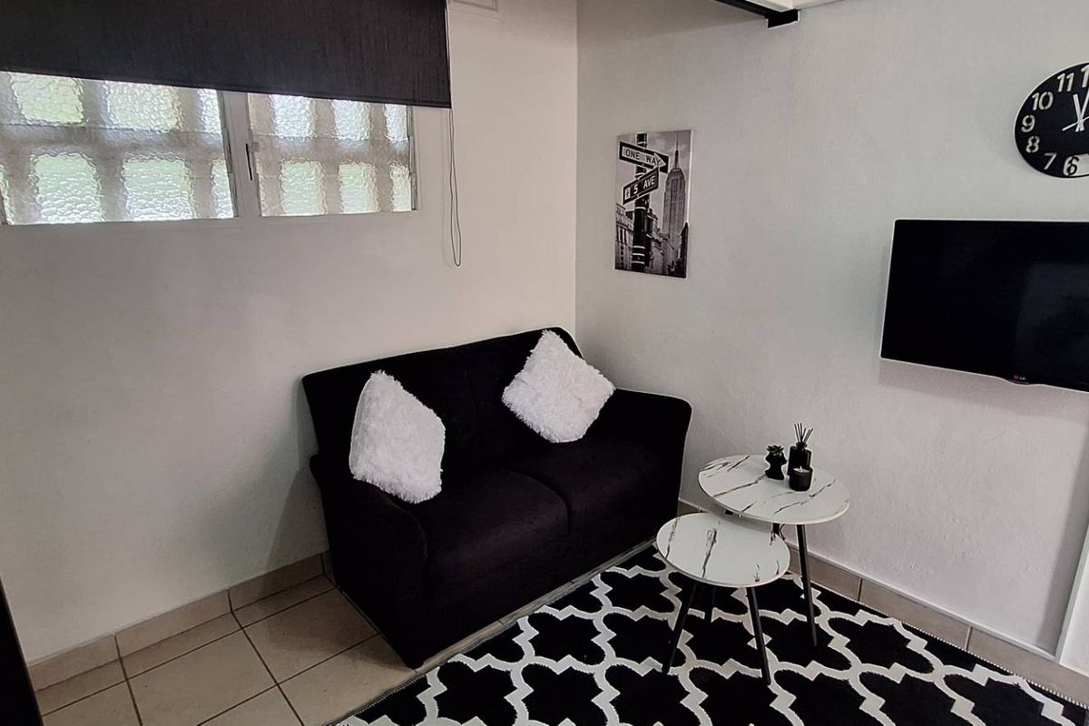 A compact living area featuring tiled flooring and a window with a roller blind, providing a functional space for relaxation.