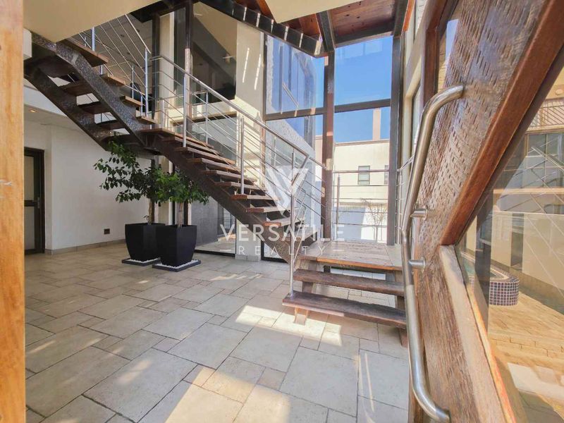 Spacious modern entrance hall featuring a striking timber staircase with stainless steel balustrades, stone flooring, and expansive floor-to-ceiling glass windows.