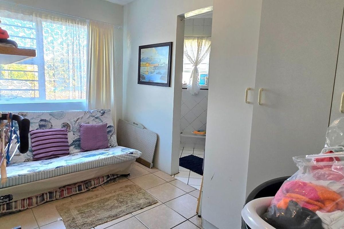 A bedroom featuring built-in cupboards, tiled flooring, and an adjoining bathroom entrance, providing a functional living space with natural light.