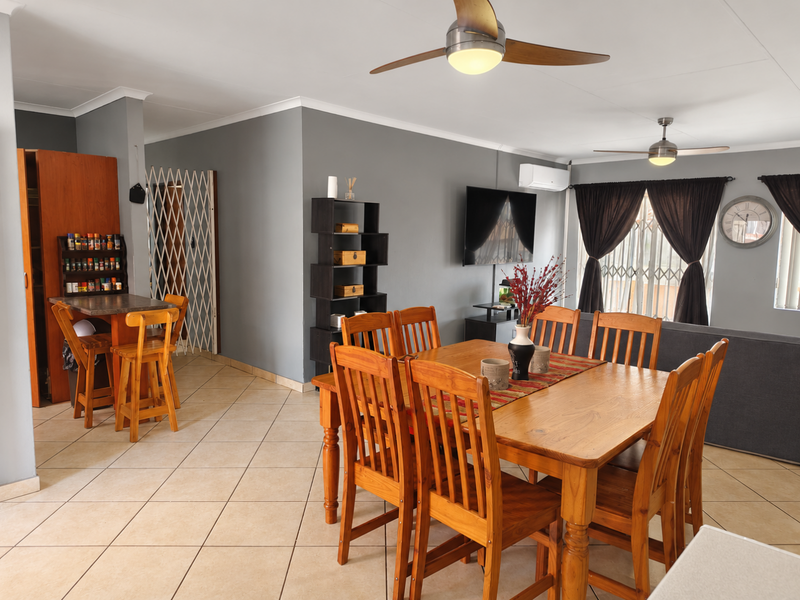 Spacious open-plan living and dining area featuring tiled flooring, ceiling fans, and a wall-mounted air conditioning unit.