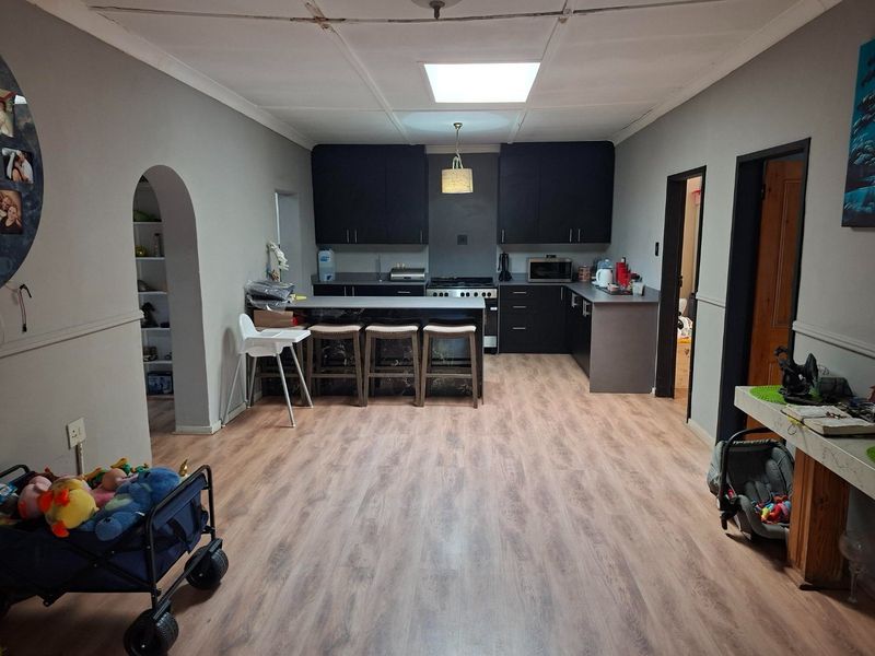 Open plan kitchen and living area featuring dark cabinetry, a breakfast bar, and wood-look laminate flooring, with an adjacent arched storage alcove.