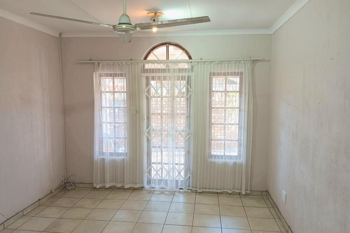 An empty living room featuring tiled flooring, a ceiling fan, and a central security gate with flanking windows.