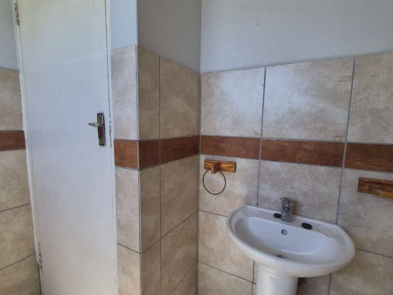 A compact bathroom featuring a pedestal basin, neutral ceramic wall and floor tiling, and a standard interior door.