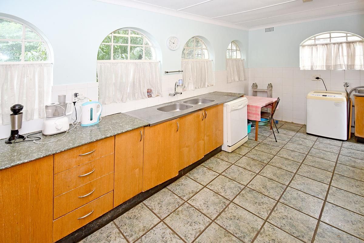 Functional kitchen featuring wooden cabinetry, double stainless steel sink, tiled splashbacks, and arched windows providing natural light.