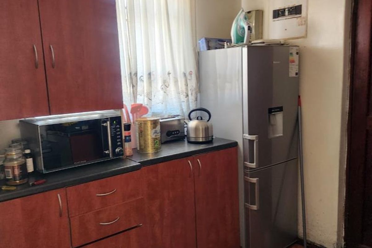 A compact kitchen featuring laminate cabinetry, dark countertops, and ceramic floor tiles, currently showing signs of wear and ceiling water damage.