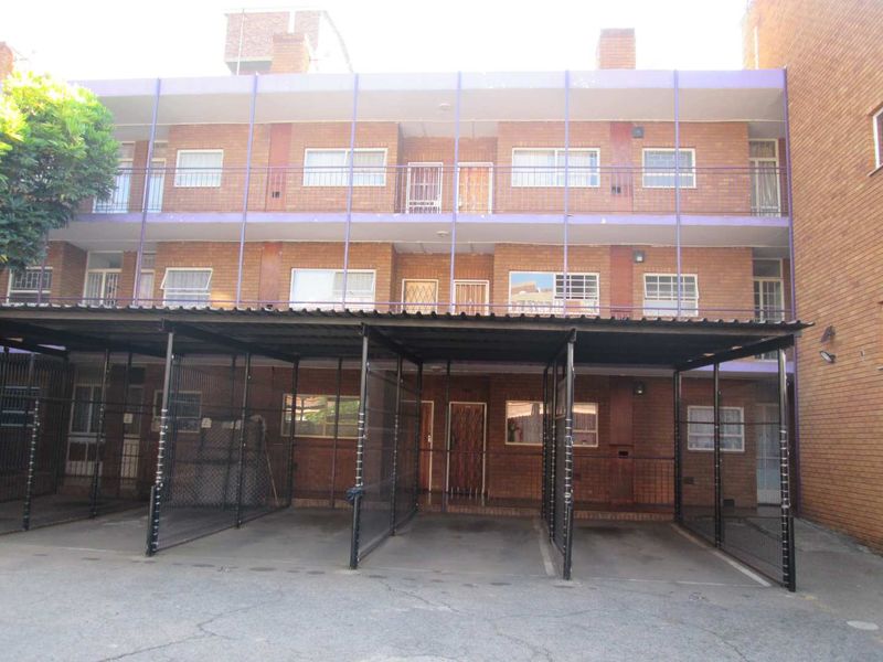 Exterior view of a multi-story apartment building featuring brick facade, covered carports, and balcony access with security gates.