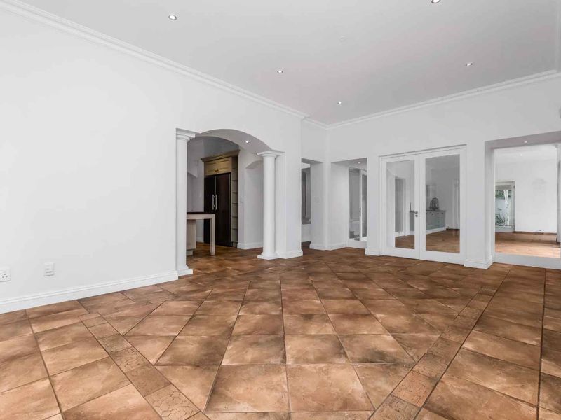 Spacious, empty living area featuring tiled flooring, decorative columns, an elegant archway, and classic crown molding, providing a bright and versatile living space.