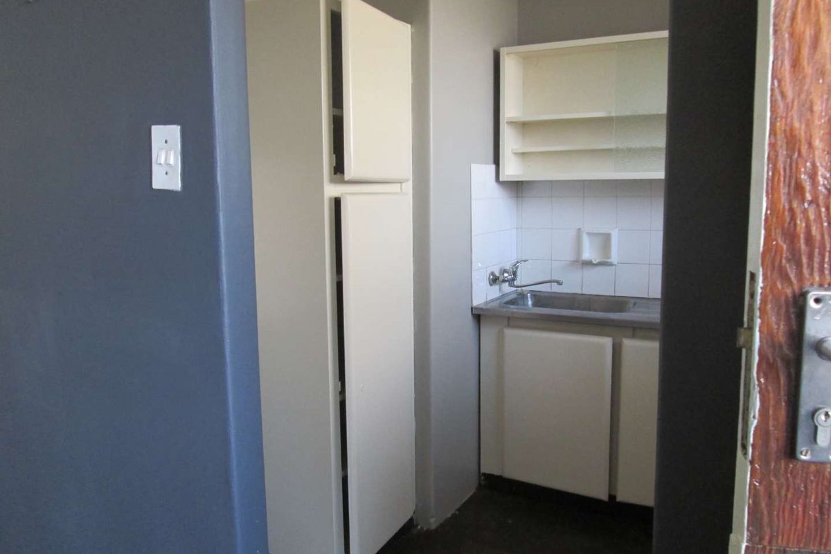 A compact, dated kitchen area featuring built-in cabinetry, a stainless steel sink, and tiled splashback, offering potential for modernization.
