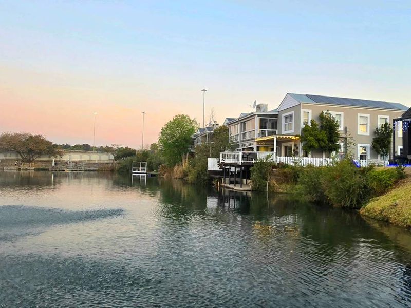 A scenic view of the rear of the property featuring a waterfront setting with a fountain, decking, and well-maintained landscaping.