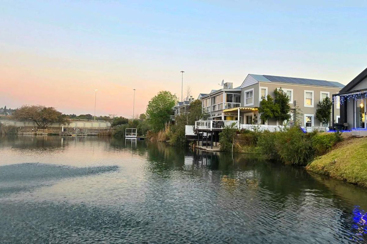 A scenic view of the rear of the property featuring a waterfront setting with a fountain, decking, and well-maintained landscaping.