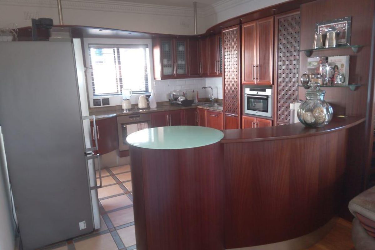 A traditional kitchen featuring dark wood cabinetry, a curved breakfast bar with a glass top, built-in oven, and tiled flooring.