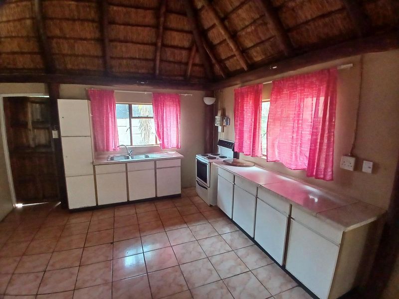 A rustic kitchen featuring a traditional thatched roof with exposed timber beams, tiled flooring, and functional built-in cabinetry with a freestanding stove.
