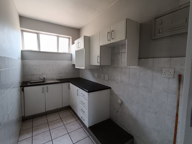 A compact kitchen featuring white cabinetry, dark countertops, tiled splashbacks, and tiled flooring. The space is currently vacant and requires minor maintenance.