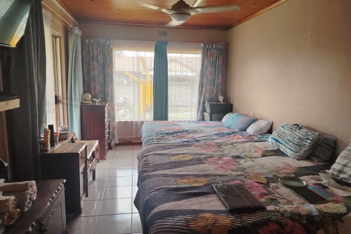 A bedroom featuring a timber-paneled ceiling, ceiling fan, and tiled flooring, offering a functional space with large windows for natural light.