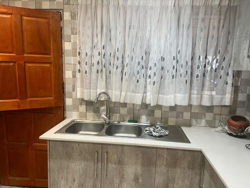 A functional kitchen area featuring a double bowl stainless steel sink, modern mixer tap, laminate cabinetry, and a tiled backsplash.