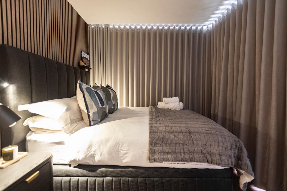 A modern bedroom featuring stylish slatted timber wall paneling and full-height floor-to-ceiling curtains, creating a cozy and sophisticated atmosphere.