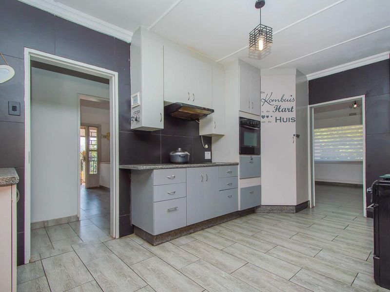 A functional kitchen featuring built-in cabinetry, granite countertops, a built-in oven, and an extractor fan, finished with modern tiled flooring.