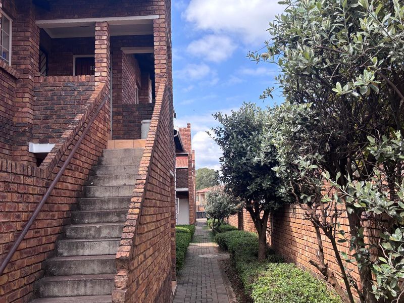 Exterior view of an apartment complex featuring face brick architecture, a concrete staircase with a metal handrail, and a paved walkway lined with mature shrubs.