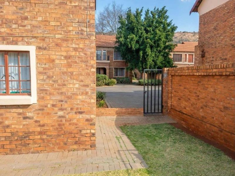 A view of the rear exterior area featuring a paved walkway, small lawn, and brick boundary wall within a residential apartment complex.