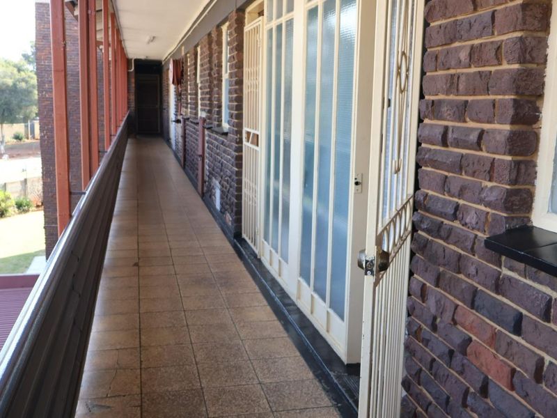 An exterior apartment hallway featuring brick walls, tiled flooring, and metal security gates providing access to the units.
