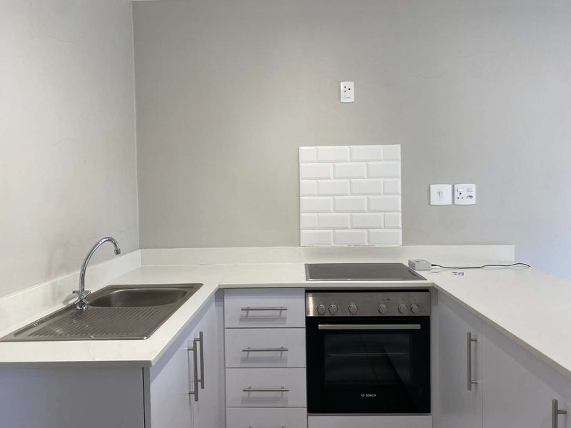 A clean, modern kitchen featuring white cabinetry, stone countertops, a stainless steel sink, and a built-in Bosch oven with an electric hob.